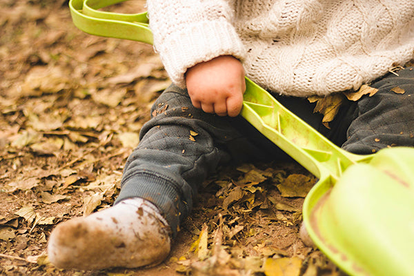 Teach kids to enjoy outdoors play: Baby sitting on soil with leaves & spade