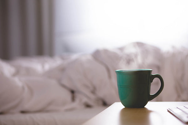 Reasons why coffee is good for your health: Green steaming coffee cup beside bed